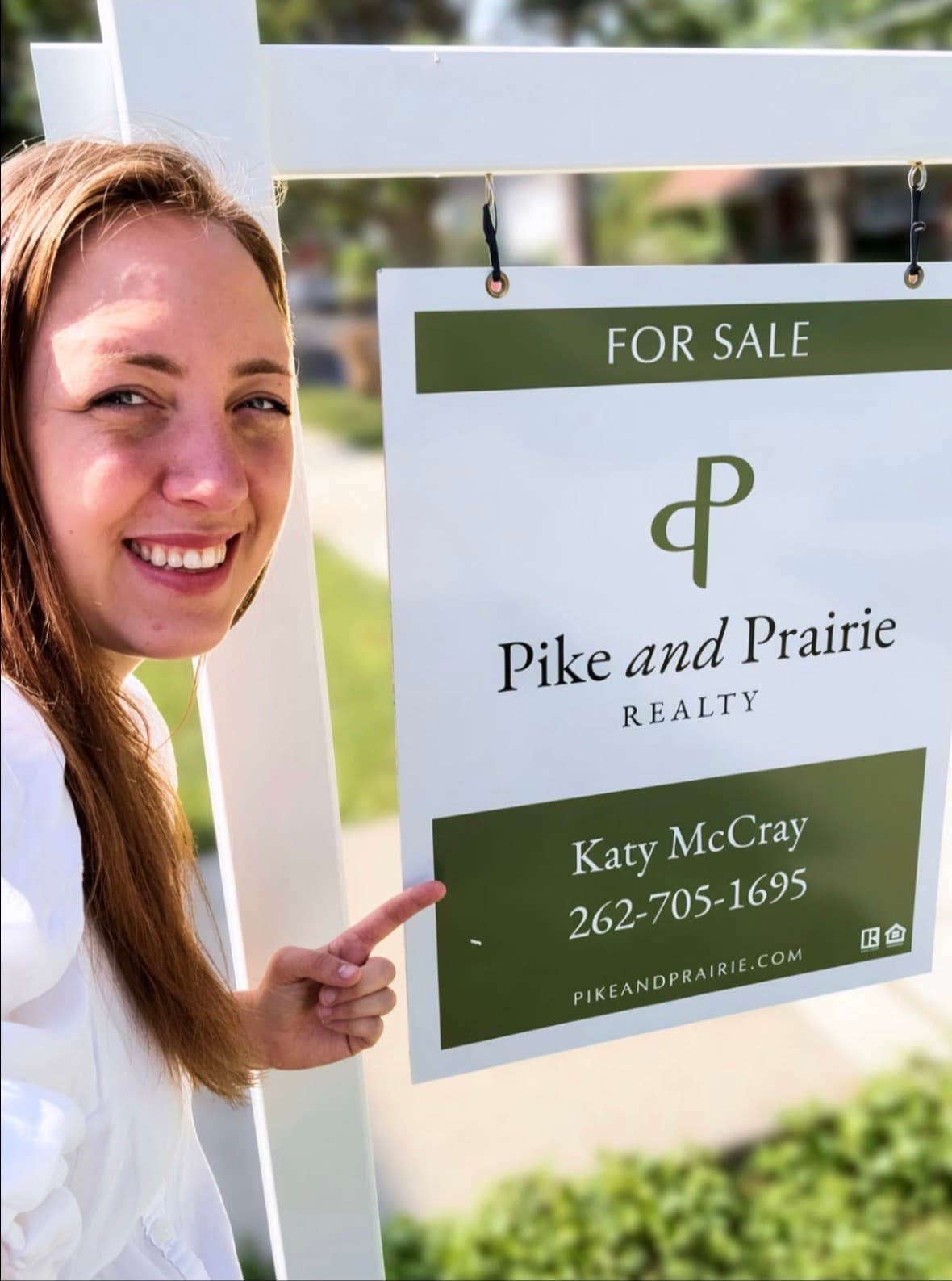 Katy McCray beside a Pike & Prairie Realty for-sale sign